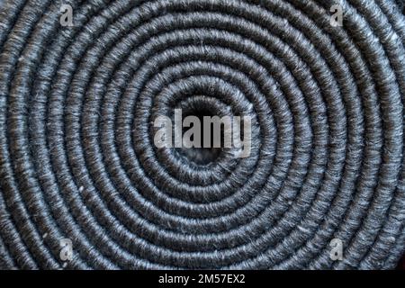 Rilievo texture di tappeto grigio arrotolato come sfondo. Primo piano di corda oscura naturale avvolta, spirale di iuta dal disegno dall'alto. Concetto di texture e sfondi. Foto Stock