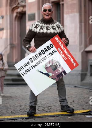 09 dicembre 2022, Hessen, Francoforte sul meno: Peter Wirth, il pilota di tram conosciuto come 'Bahnbabo', è in piedi con un poster elettorale davanti al Römer di Francoforte. Il 61-year-old vuole correre come candidato alle nuove elezioni per il sindaco il 5 marzo 2023. (A dpa 'anche il 'Bahnbabo' c'è - candidati indipendenti in OB elezione') Foto: Boris Roessler/dpa Foto Stock