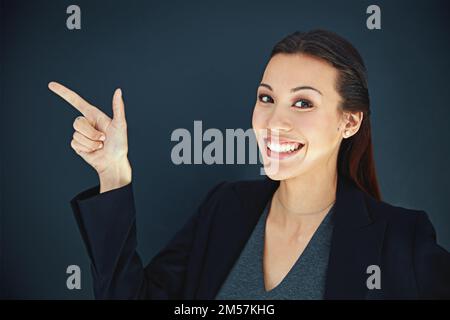 La strada verso il successo è questa. Ritratto di una giovane donna d'affari che punta al lato su uno sfondo scuro. Foto Stock
