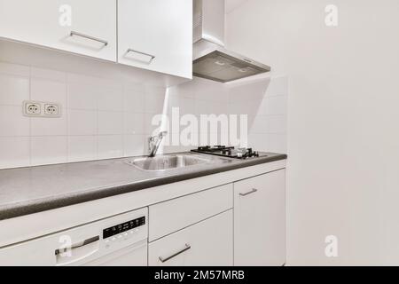 una cucina con armadi bianchi e ripiani neri sui banchi di fronte alla lavastoviglie c'è un apparecchio Foto Stock