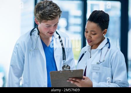 Collaborazione per un'assistenza sanitaria di alta qualità. due giovani medici che discutono di una cartella pazienti. Foto Stock