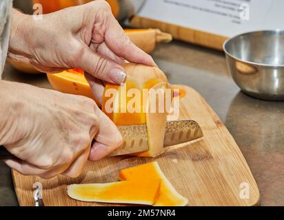 Lo chef taglia la zucca a forma di pera su un asse di legno nella cucina casalinga Foto Stock