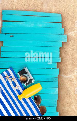 Asciugamano a strisce blu e bianco con macchina fotografica, bottiglia gialla, stella marina, occhiali da sole su tavole di legno, molo. Piscina, spiaggia, mare. Verticale, orizzontale. Vacanza Foto Stock