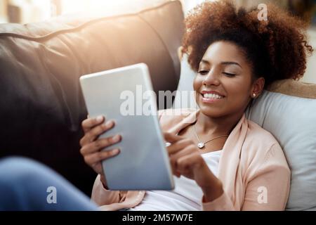 Ricerca di nuovi aggiornamenti nell'account dei social media. una giovane donna rilassata che usa un tablet digitale sul divano a casa. Foto Stock