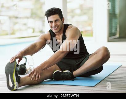 Godendo di un tratto soddisfacente. Ritratto di un giovane che si allunga prima del suo allenamento a casa. Foto Stock