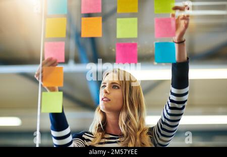 Il brainstorming incoraggia nuovi modi di pensare. una giovane donna che ha una sessione di brainstorming con note appiccicose al lavoro. Foto Stock