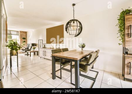 una sala da pranzo con un tavolo, sedie e piante sulla parete di fronte al soggiorno è pavimento in piastrelle bianche Foto Stock