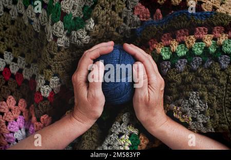 Mani da donna con palla di fili di maglia sullo sfondo di maglia a plaid Foto Stock