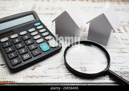 White Model House con lente d'ingrandimento e calcolatrice su sfondo in legno, concetto immobiliare Foto Stock