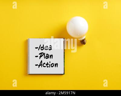 Le parole idea, piano e azione su blocco note con una lampadina. Piano d'azione di affari o concetto creativo di strategia di pianificazione di idea. Foto Stock