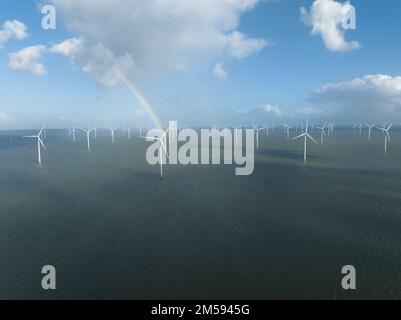 Turbina eolica offshore in mare. Generazione di elettricità in acqua aperta. Vento acqua nuvole cielo blu e un arcobaleno. Vista aerea del drone. Foto Stock