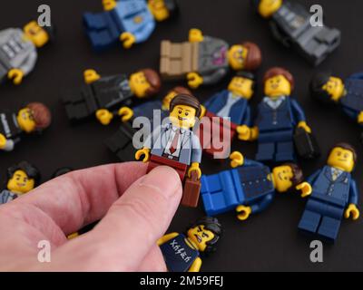 Tambov, Federazione Russa - 09 ottobre 2022 Una mano che tiene una figura di uomo d'affari Lego contro un mucchio di figura minifima, che sono giacenti su una ba nera Foto Stock