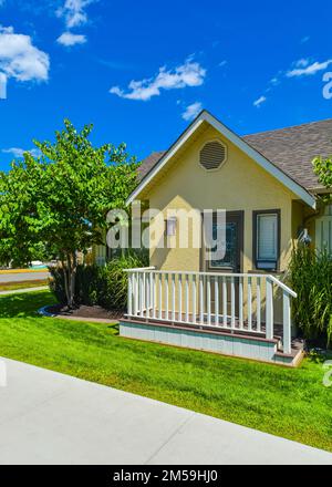 Piccola casa di famiglia gialla nelle giornate di sole con prato verde e sentiero in cemento Foto Stock