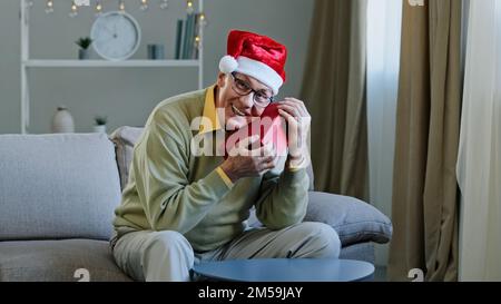 Vecchio caucasico anziano nonno maturo 60s uomo nonno maschio a Natale X-mas Santa festive cappello rosso a casa tenendo abbracciare abbraccio presente pacco Foto Stock
