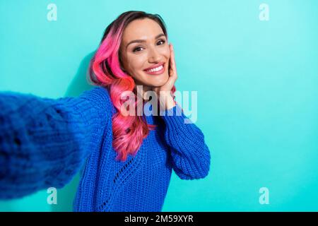 Primo piano selfie foto cadre di giovane affascinante ragazza hipster indossare blu maglia jumper touch guancia prendere shot guardare si isolato su sfondo di colore ciano Foto Stock