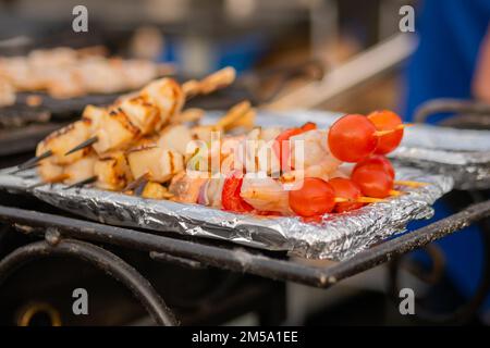 Capesante e gamberi cotti, spiedini di gamberi, pomodori ciliegini su un foglio - cibo di strada Foto Stock