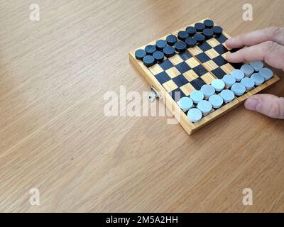 Scacchiera con dama - Pianificazione di strategia di affari. Scacchiera in plastica su tavolo di legno marrone, mano uomo adulto Foto Stock