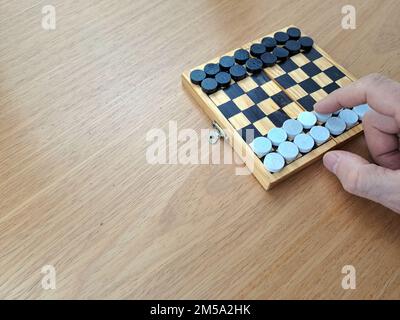 Scacchiera con dama - Pianificazione di strategia di affari. Scacchiera in plastica su tavolo di legno marrone, mano uomo adulto Foto Stock