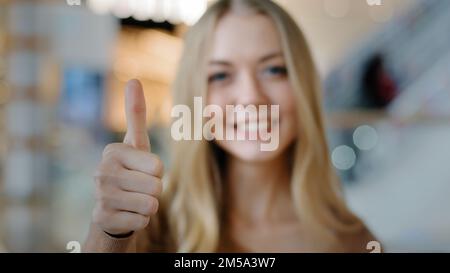 Primo piano ritratto di giovane ragazza sorridente in centro commerciale felice donna soddisfatta mostrando pollice in su guardando la macchina fotografica che dà il servizio o le merci positivi Foto Stock