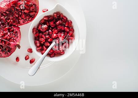 Frutti di melograno sani e maturi, aperti e spelati con semi su piatto bianco Foto Stock