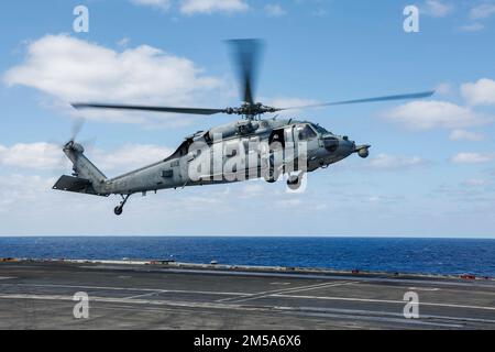 MARE DELLE FILIPPINE (15 febbraio 2022) un elicottero MH-60s Sea Hawk, assegnato ai “Chargers” di Helicopter Sea Combat Squadron (HSC) 14, si prepara ad atterrare sul ponte di volo della portaerei di classe Nimitz USS Abraham Lincoln (CVN 72) a sostegno di Jungle Warfare Exercise 22 (JWX 22) in Okinawa, Giappone. JWX 22 è un'esercitazione di formazione sul campo su larga scala incentrata sull'utilizzo delle capacità integrate di partner congiunti e alleati per rafforzare la consapevolezza, la manovra e gli incendi in tutti i settori in un ambiente marittimo distribuito. Foto Stock