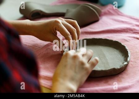 Primo piano immagine delle mani femminili opere con argilla rende futuro piastra in ceramica, classi di costruzione a mano in laboratorio di ceramica moderna, artigianato creativo Foto Stock