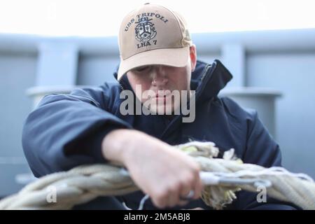 220215-N-TT639-1031 OCEANO PACIFICO (15 febbraio 2022) – Seaman Jackson Bumgardner, di San Antonio, esegue un controllo di manutenzione su una delle linee di ormeggio delle navi d’assalto anfibie USS Tripoli (LHA 7), 15 febbraio. Tripoli sta conducendo operazioni di routine nella U.S. 3rd Fleet. Foto Stock