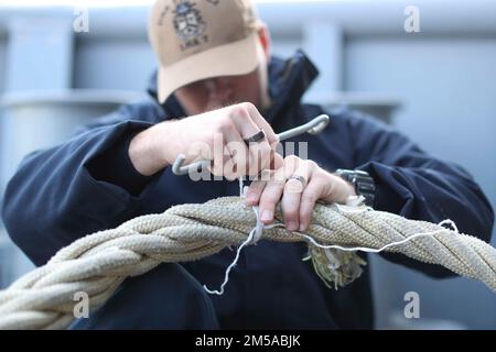 220215-N-TT639-1029 OCEANO PACIFICO (15 febbraio 2022) – Seaman Jackson Bumgardner, di San Antonio, esegue un controllo di manutenzione su una delle linee di ormeggio delle navi d’assalto anfibie USS Tripoli (LHA 7), 15 febbraio. Tripoli sta conducendo operazioni di routine nella U.S. 3rd Fleet. Foto Stock