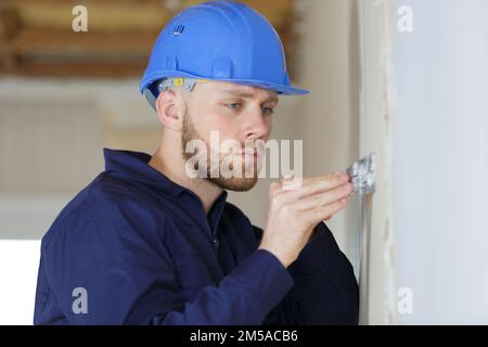 costruttore maschio con coltello stucco su parete bianca Foto Stock