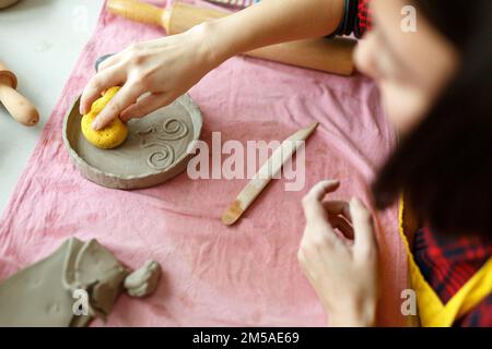 Le mani femminili lavorano con Clay rende la piastra ceramica del futuro, classi di costruzione manuale in officina di ceramica moderna, persone creative Design artigianale Foto Stock