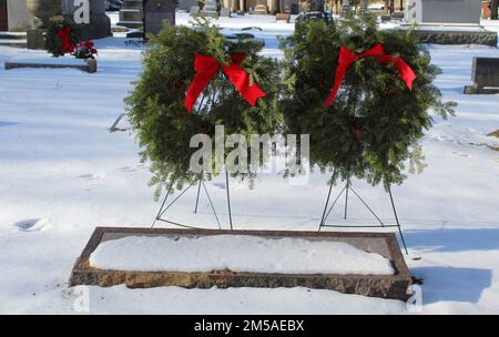 Due corone natalizie dietro una lapide in un cimitero suburbano di Chicago con la neve Foto Stock