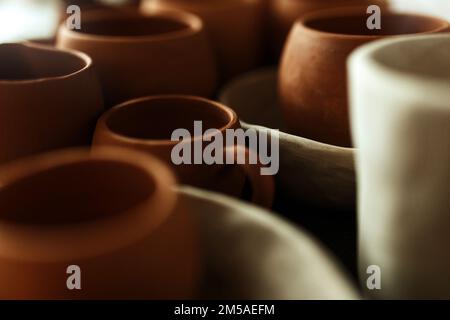 Un primo piano di varie stoviglie di argilla che asciugano su uno scaffale. Un concetto di studio di ceramica. Piatti artigianali, ciotole, pentole, tazze di diversi colori. Vista accogliente Foto Stock