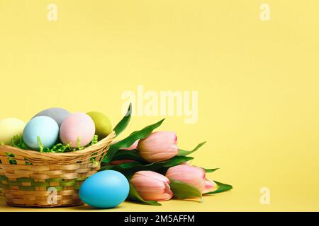 Cestino con uova di Pasqua fiori tulipani sul tavolo. Spazio di copia per primo piano ancora esaurito Foto Stock