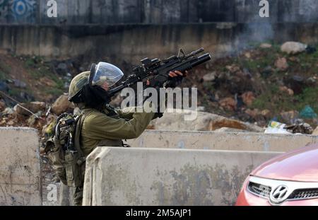 Ramallah. 27th Dec, 2022. Un soldato israeliano punta la sua arma contro i manifestanti palestinesi durante gli scontri al checkpoint di Qalandia, vicino alla città di Ramallah, in Cisgiordania, il 27 dicembre 2022. Credit: Nidal Eshtayeh/Xinhua/Alamy Live News Foto Stock