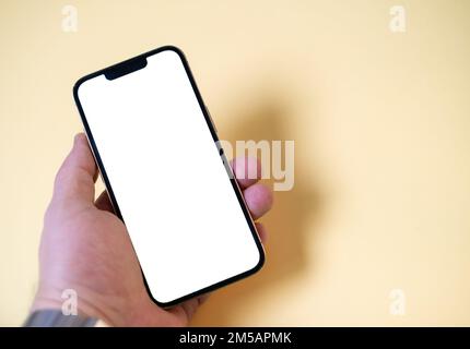 Mano che tiene nero smartphone isolato su sfondo giallo, sfondo bianco schermo. Mano che tiene in mano uno smartphone con schermo verde, vuoto, spazio per la copia. Foto Stock