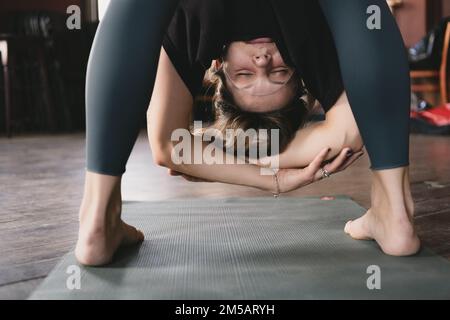 Foto ravvicinata di una nuova insegnante di yoga femminile che fa una piega in piedi avanti posa variazione mani a gomito, posa penzolante (uttanasana) durante la sua vinyasa Foto Stock