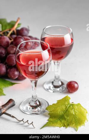 Due bicchieri di vino rosso o rosa, un mazzo di uve rosse e cavatappi, ancora vita su sfondo grigio chiaro. Celebrazione per due concetto. Verticale ori Foto Stock