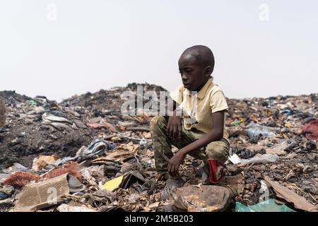 Piccolo ragazzo africano circondato da mucchi di lettiera domestica; concetto di gestione dei rifiuti irrisolti nei paesi del terzo mondo Foto Stock