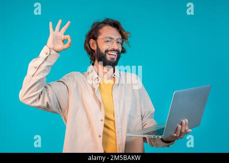 Ritratto di un uomo che tiene un computer portatile e celebra il successo isolato su sfondo blu Foto Stock