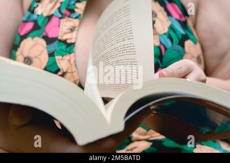 primo piano vista frontale di un libro spesso aperto tenuto da una donna caucasica irriconoscibile che sta leggendo e girando la pagina Foto Stock