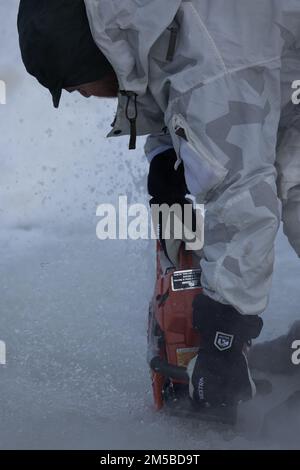 Un Beret Verde assegnato a 10th Special Forces Group (Airborne) apre un'apertura in un lago ghiacciato con una motosega per condurre un addestramento di sopravvivenza alle basse temperature presso la Yukon Training Area, Alaska, 19 febbraio 2022. ARCTIC EDGE è un'azienda statunitense Northern Command esercizio progettato per dimostrare e testare la capacità di dispiegarsi rapidamente e operare in condizioni artiche. Foto Stock