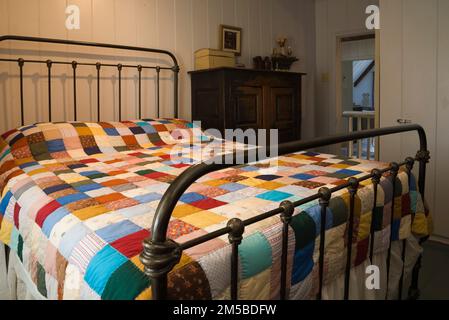 Antico letto matrimoniale in ottone coperto con trapunta patchwork nella camera da letto principale al piano superiore all'interno della vecchia casa in stile regime francese del 1772. Foto Stock