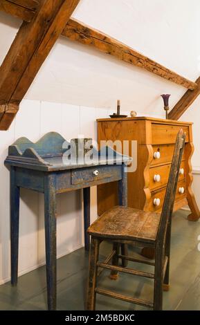 Scrivania di antiquariato in legno blu e sedia con schienale alto e comò nella camera principale degli ospiti al piano superiore all'interno di una vecchia casa in stile regime francese del 1722. Foto Stock