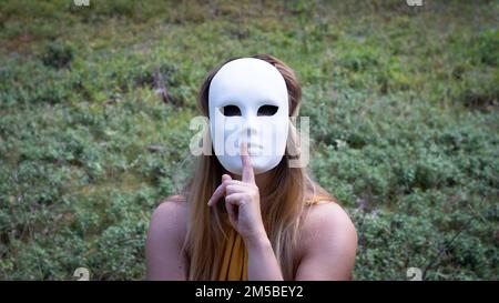 Donna con una maschera Columbine seduta nella foresta Foto Stock