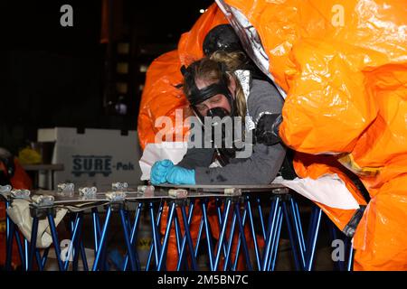 I membri del team di supporto civile delle 32nd armi di distruzione di massa della Guardia Nazionale del Maryland rimuovono la tuta di livello A di Kim Kerschner di Classe 1st durante lo scenario di incidente di un esercizio di addestramento sul campo di agenti a base farmaceutica presso la Quinta armeria Regiment a Baltimora, il 23 febbraio 2022. Il CST 32nd utilizza questo tipo di esercizio per addestrarsi in modo che siano sempre pronti a sostenere le autorità civili in un incidente chimico domestico, biologico, radiologico o nucleare Foto Stock