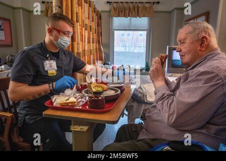 STATI UNITI Robert D. VonScheven, Bravo Company, 104th Brigade Engineer Battaglione, 44th Fanteria Brigade Combat Team, New Jersey Army National Guard, assiste Charles Riley, residente presso la New Jersey Veterans Memorial Home a Vineland, con il suo pranzo a Vineland, New Jersey, 24 febbraio 2022. VonScheven sta servendo i residenti della casa come assistente infermieristico certificato. Più di 70 soldati della Guardia Nazionale del New Jersey e Airmen stanno servendo come assistenti infermieristici certificati e in servizi alimentari, controllo delle infezioni, tecnologia dell'informazione, arricchimento della vita, Logistica, E COVID-19. (Nuovo Jers Foto Stock