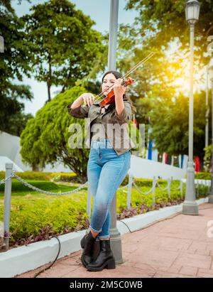 Donna che suona il violino per strada. Ritratto di una ragazza violinista che suona per strada. Artista donna che gioca violino all'aperto, ragazza sdraiata che gioca Foto Stock