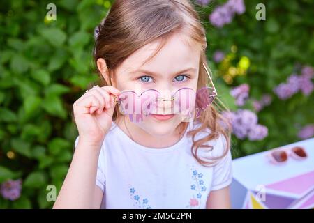 Cute ragazza sorridente bambino 3-5 anni capelli lunghi in posa all'aperto su sfondo naturale. Guardando la fotocamera. Stagione primaverile. Infanzia. Foto Stock