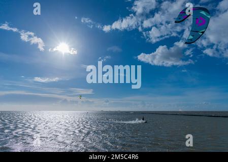 Kitesurf sul Mare del Nord, Luettmoorsiel, Reussenkoege, all'orizzonte Hallig Nordstrandischmoor, Lorendamm, retroilluminazione, forza del vento 6, cielo blu Foto Stock