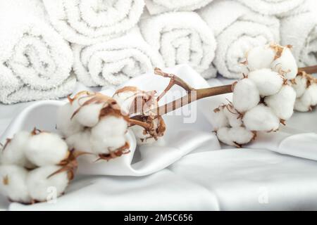 Bastoncini di cotone su raso bianco e asciugamani arrotolati sullo sfondo, messa a fuoco morbida primo piano Foto Stock